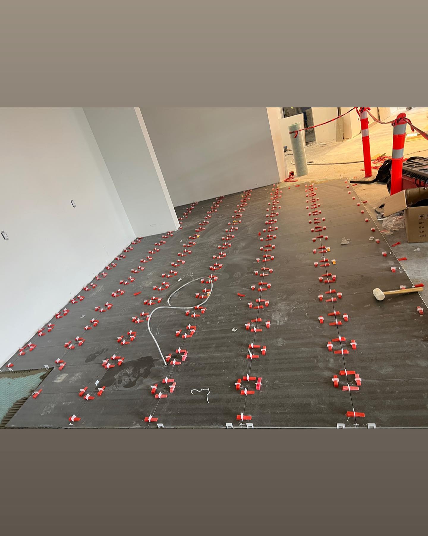 Dark rectangular floor tiles are set out with visible levelling clips in an interior under construction.