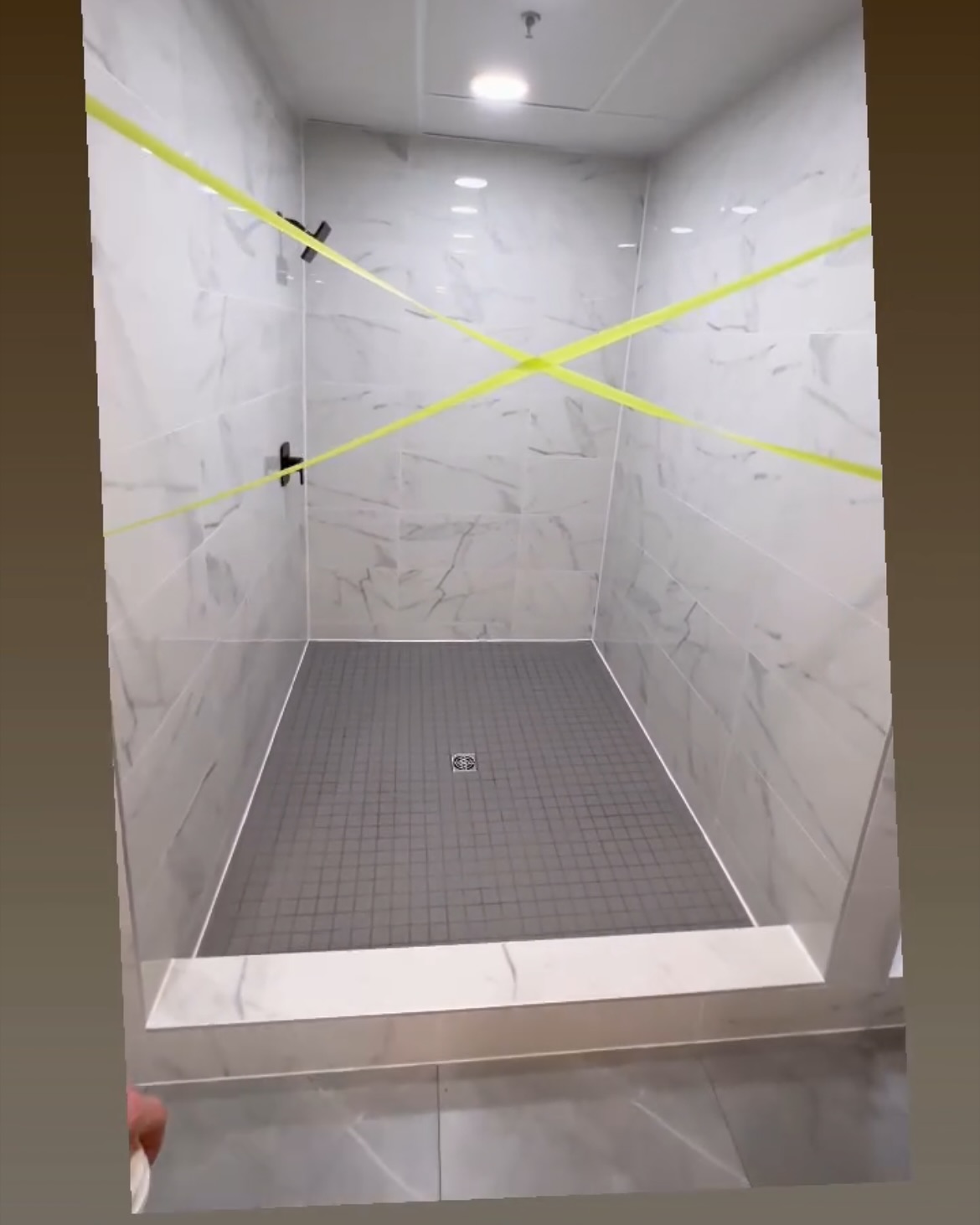 Broad, pale wall tiles with grey veining frame a square mosaic shower base and tiled threshold. Shown in progress.
