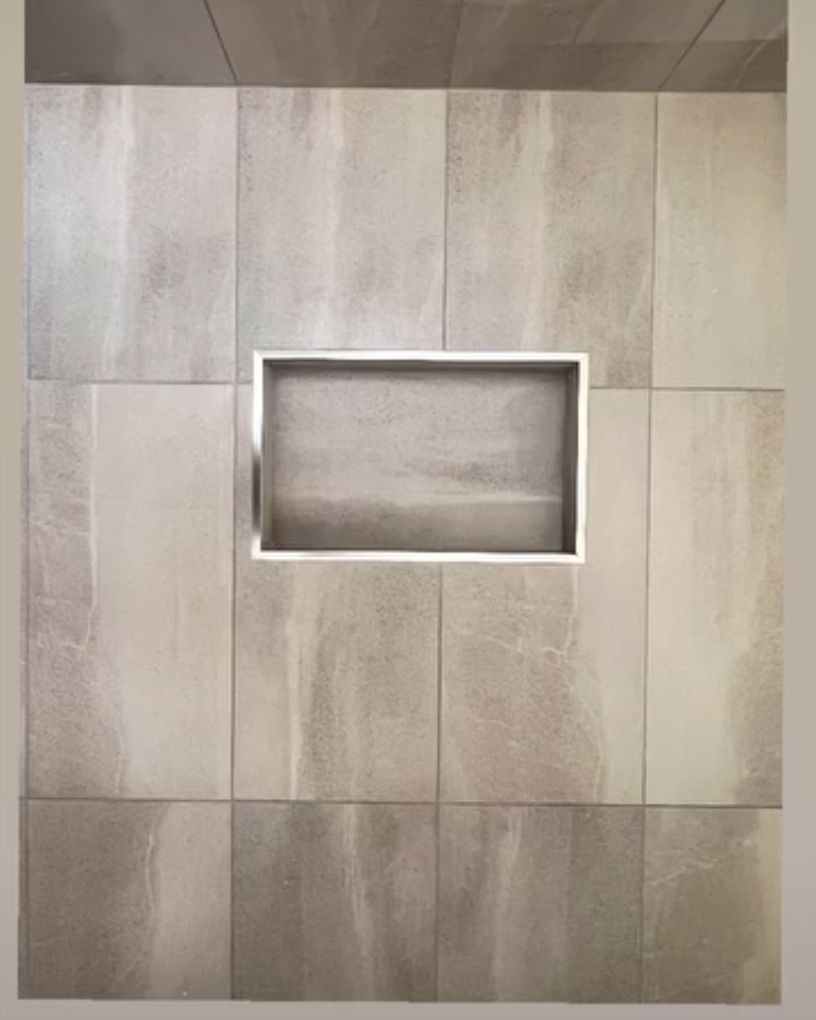 A long, metal-trimmed niche sits within a textured, vertically arranged tile wall.