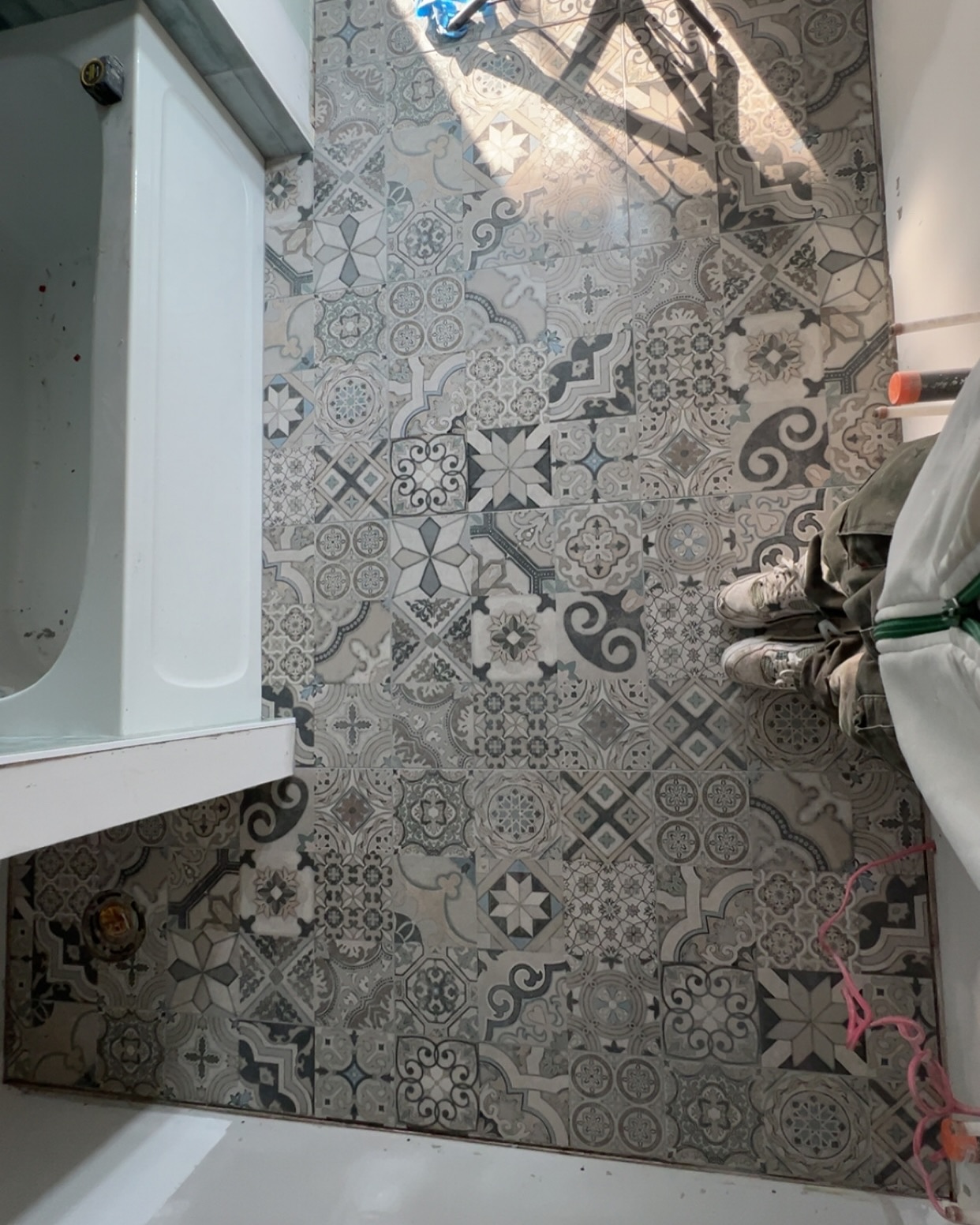 Grey and cream decorative floor tiles bring a patchwork of geometric motifs alongside the tub. Shown during installation.