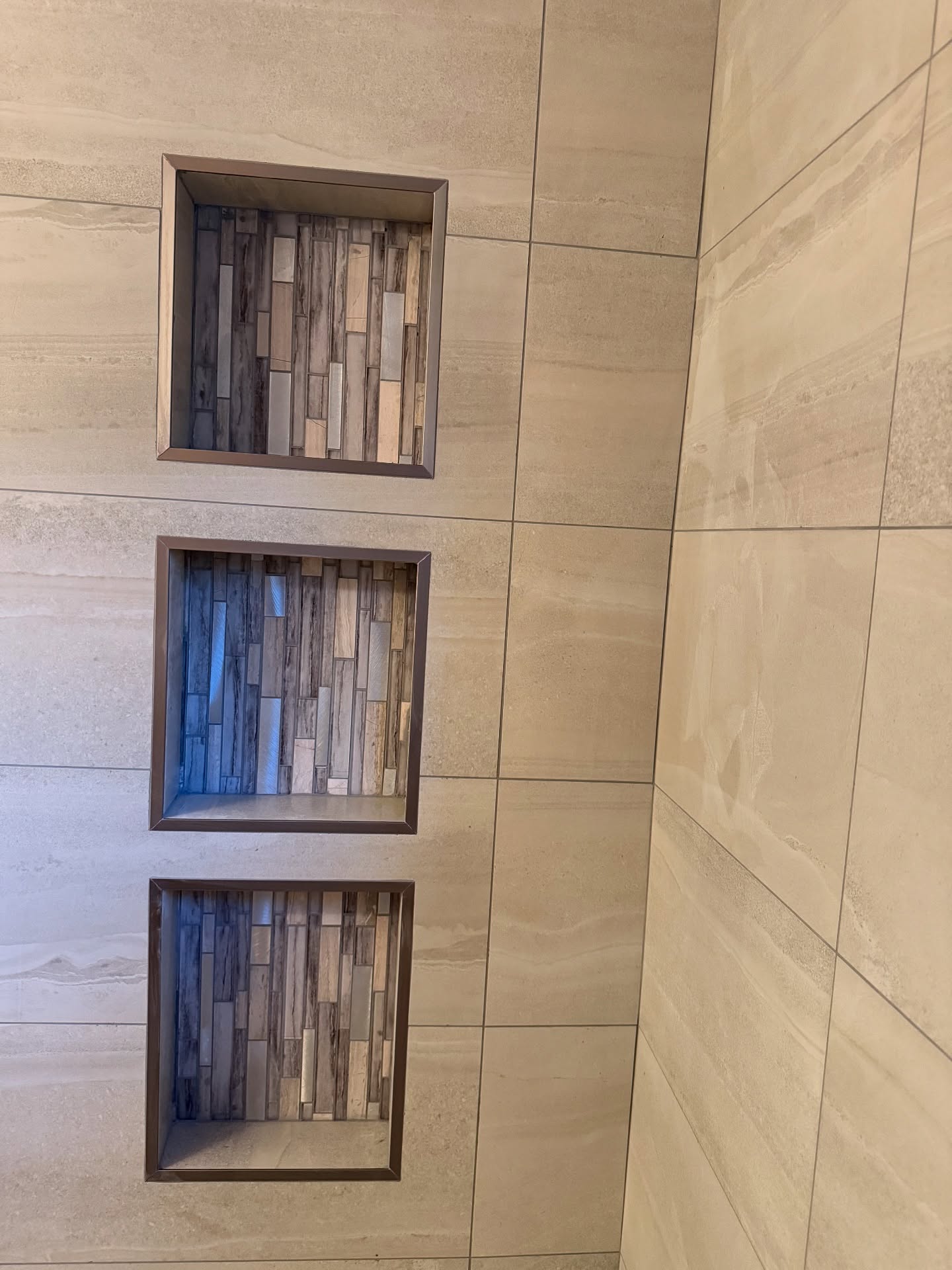 Three stacked niches pair large beige wall tiles with narrow mosaic accents and metal trim.