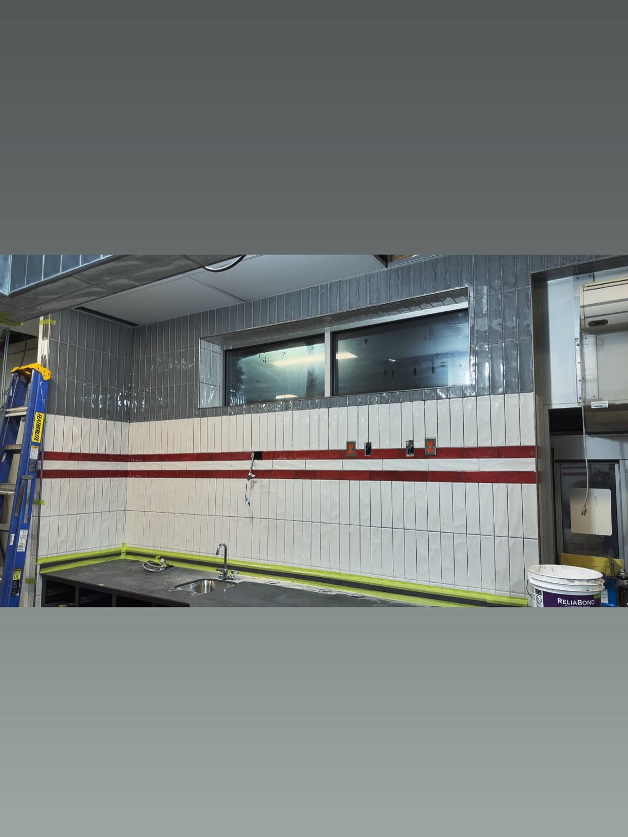 White vertical tiles and two red accent lines run beneath a blue-grey upper section and around the window reveal. Shown in progress.