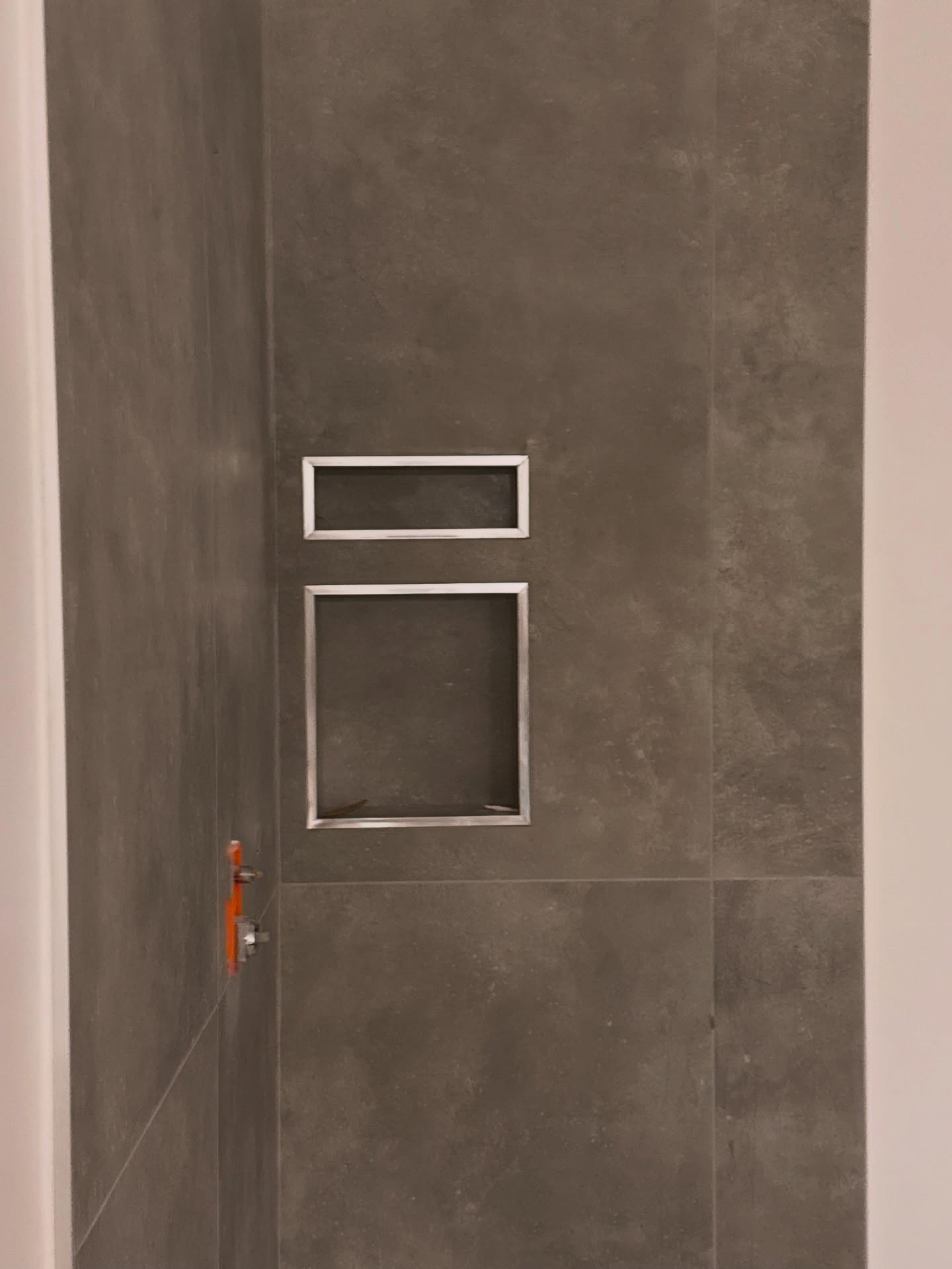 Two stacked recesses stand out against a dark, large-format shower wall with light-coloured trim. Shown in progress.