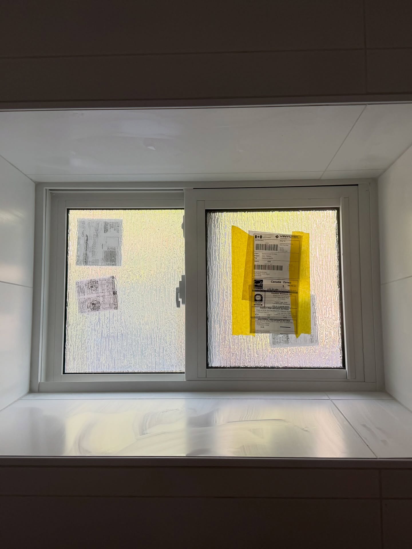 Veined pale tile wraps the sill and inner edges of a frosted window. Shown before finishing.