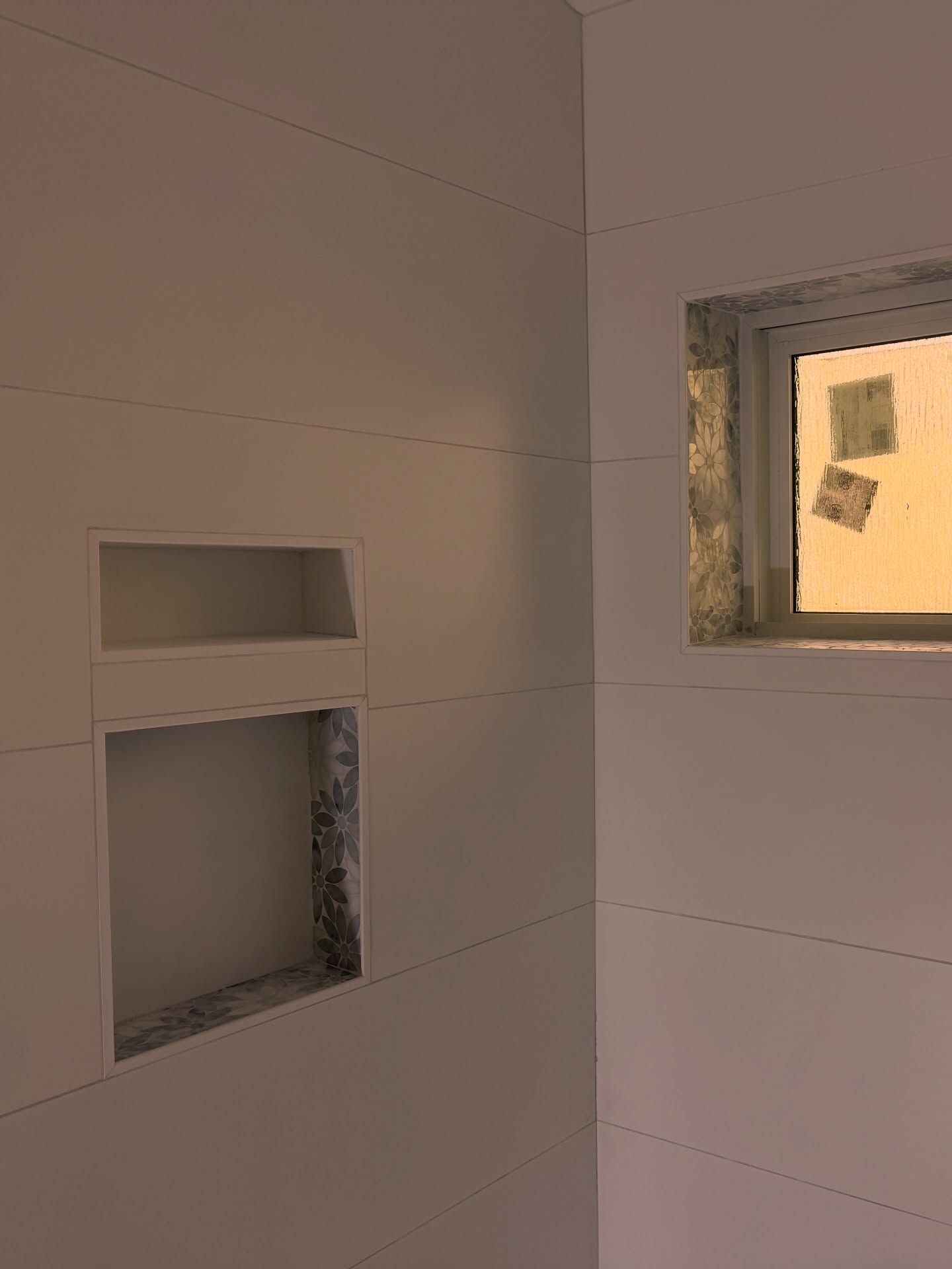 Light rectangular wall tile, stacked niches and a mosaic inset meet around a shower window.