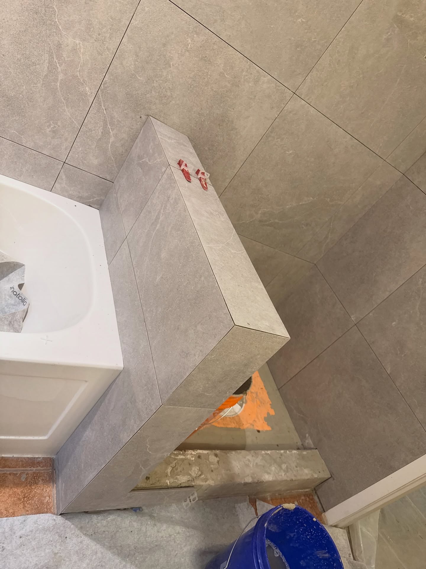 Beige tile continues across a wall, ledge and boxed return, with visible levelling clips during installation.