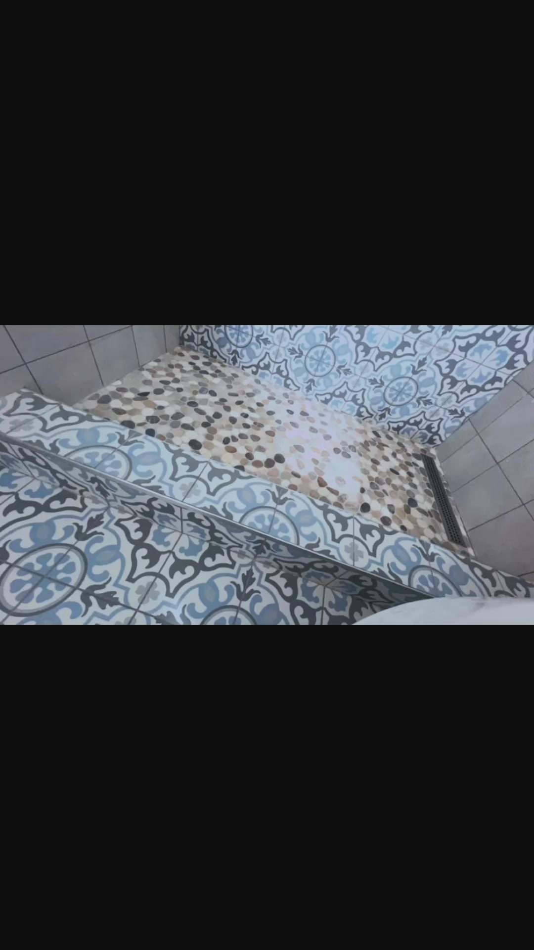 Decorative patterned tile meets a pebble-style shower floor at the shower entrance.