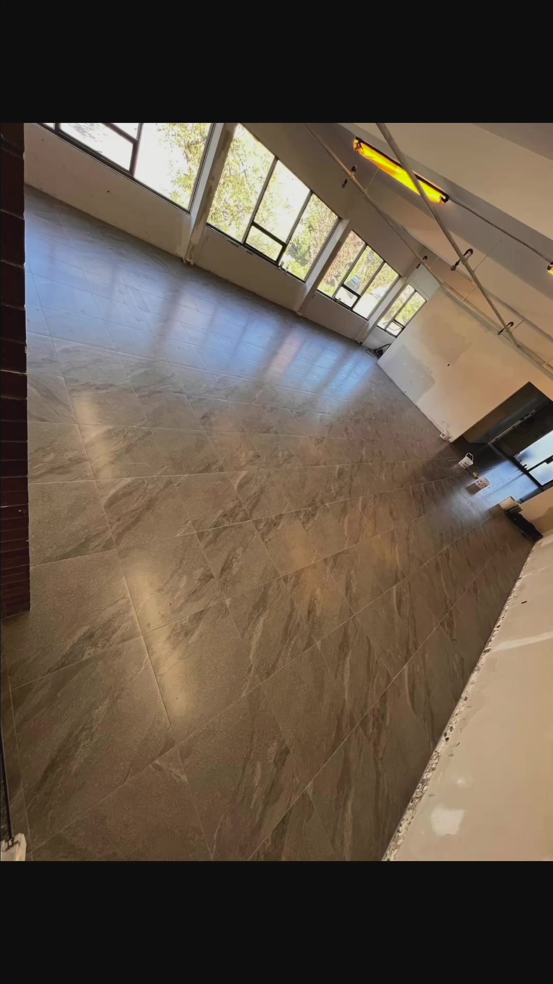 Large rectangular stone-look floor tiles extend through a bright room during renovation.