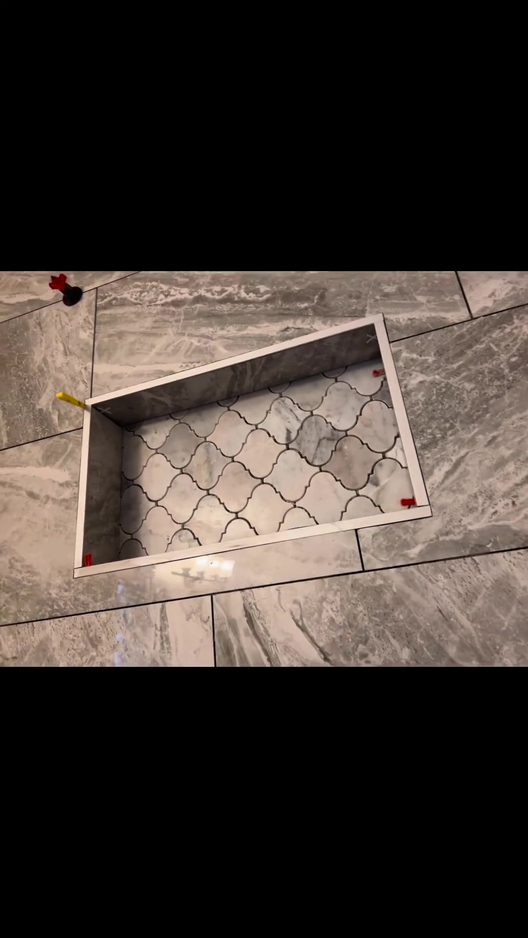 A metal-trimmed niche combines an arabesque mosaic back with surrounding grey stone-look wall tiles. Shown in progress.