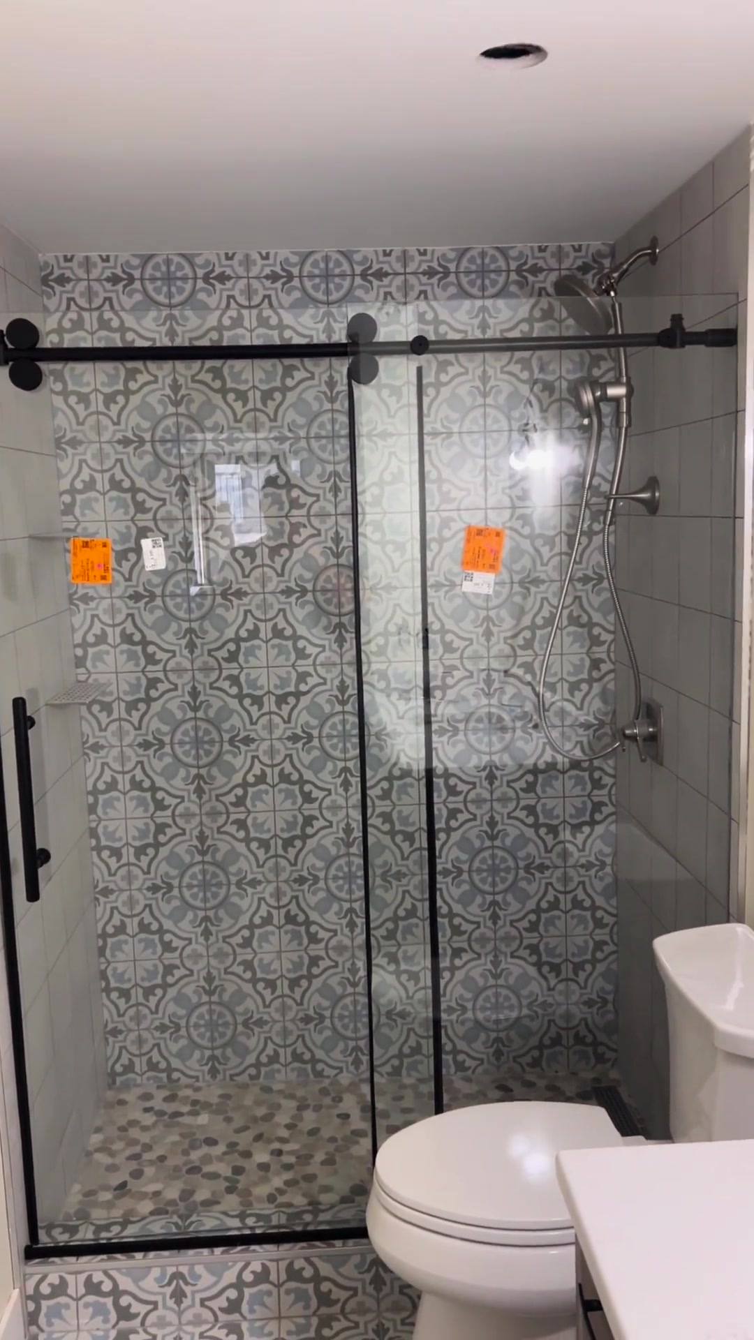 Decorative wall tiles, a pebble-style shower base and dark sliding-door hardware create a layered bathroom finish.