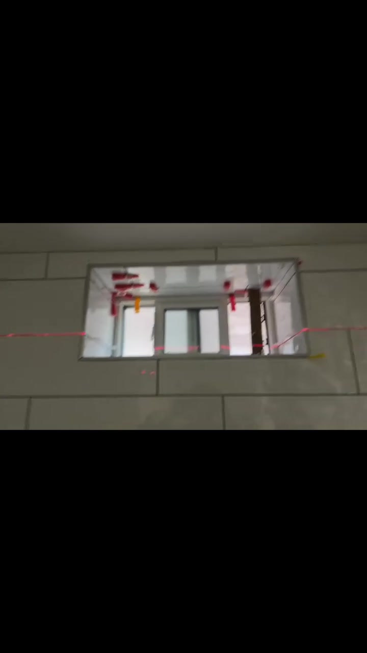 Horizontal rectangular wall tiles meet a recessed window while a visible laser line guides the installation.