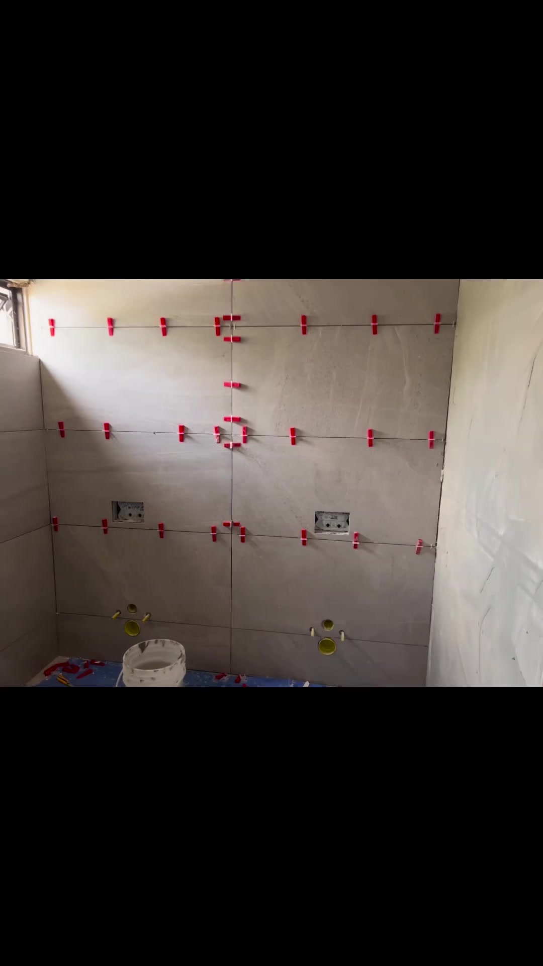 Large, pale wall tiles are shown during setting, with levelling clips holding the joints.