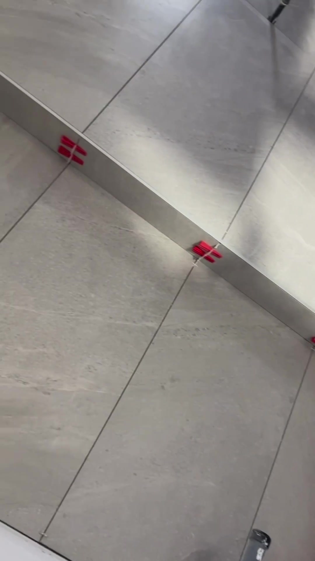 Pale tile wraps the raised shower curb and adjoining surfaces, with clips still in place during installation.