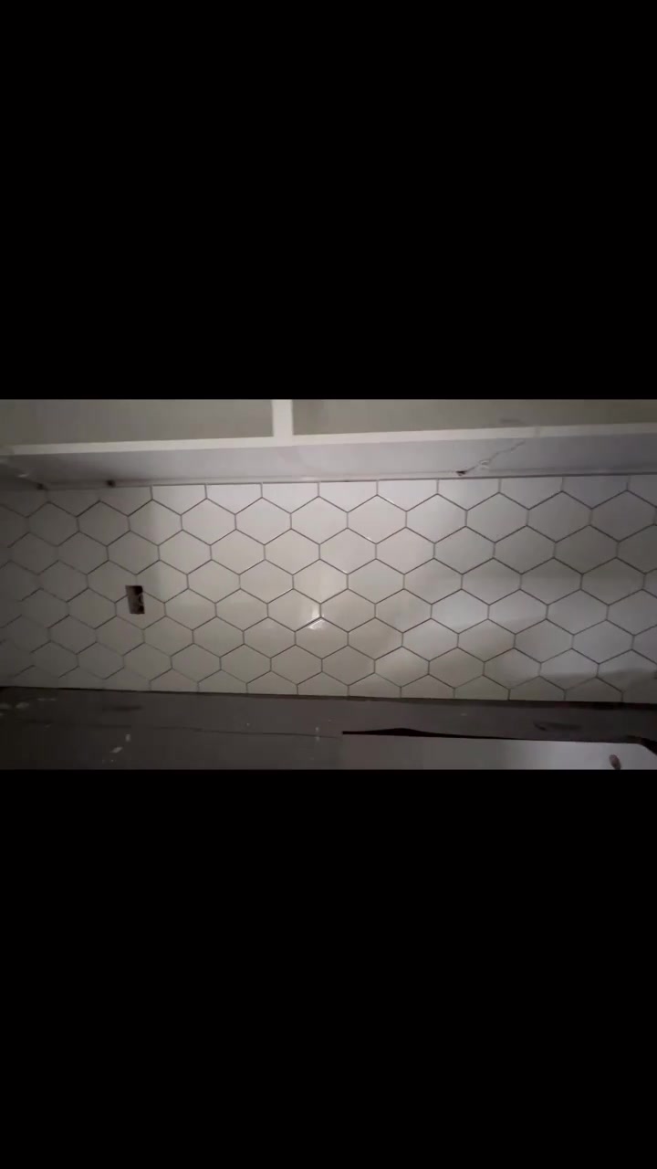 Light hexagonal tiles span the kitchen backsplash beneath white cabinets. Shown before the outlet covers are fitted.