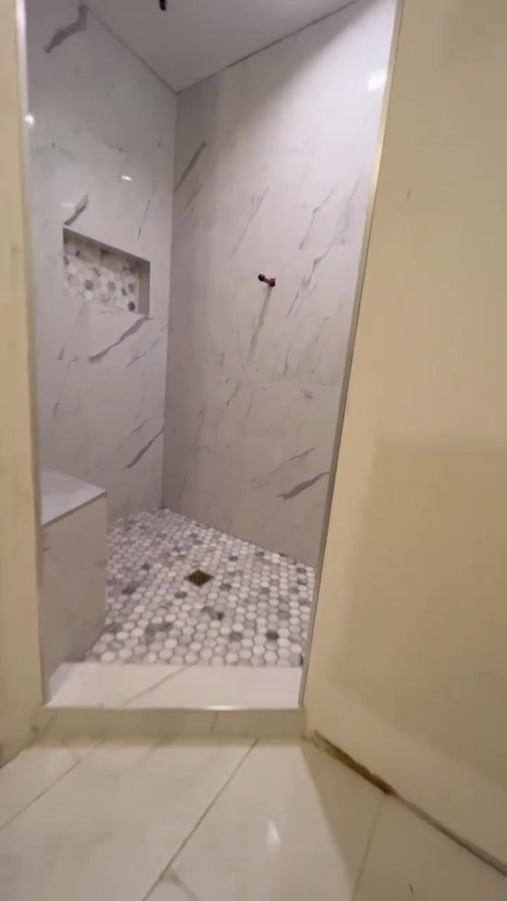 Veined wall tile, a recessed mosaic niche and a mixed-tone hexagonal base define this compact shower. Shown before final fixtures.