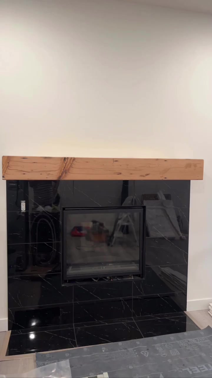 Glossy dark tile with pale veining wraps the fireplace surround and hearth beneath a timber mantel.