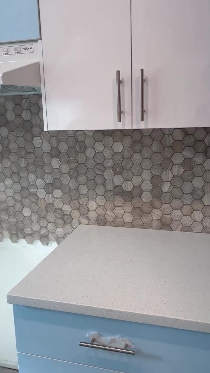A warm, varied hexagonal mosaic sits between pale countertops and white upper cabinets.