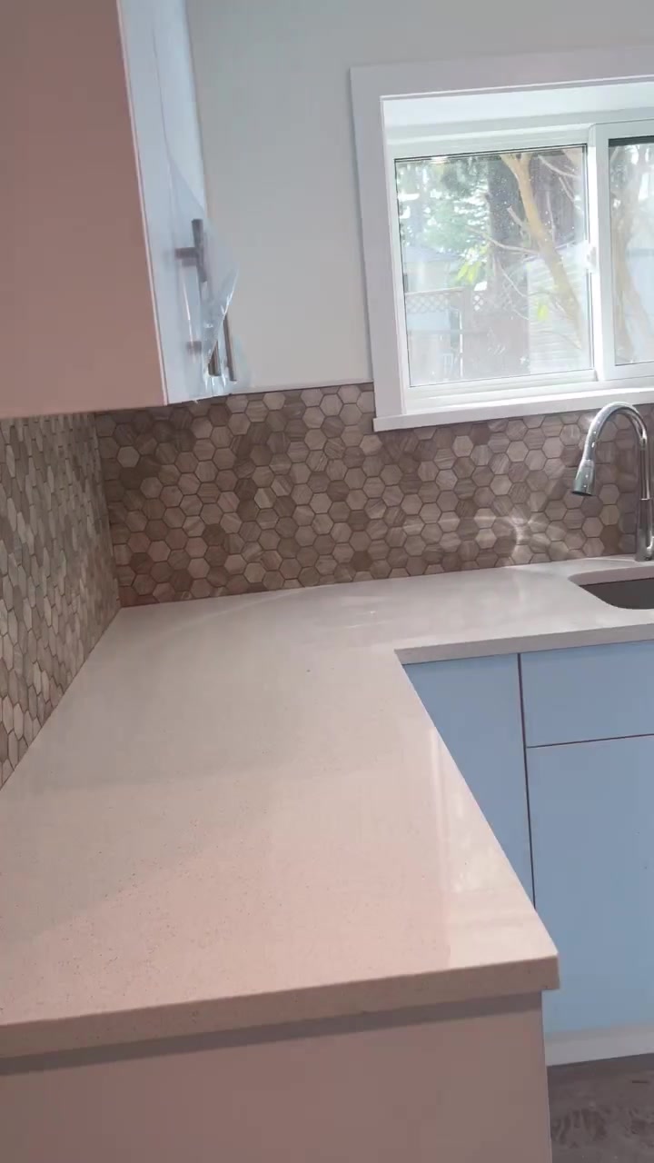 Hexagonal mosaic continues around the kitchen corner and below the window, meeting a light countertop.