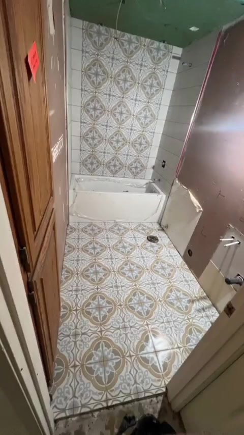 Decorative patterned tiles continue from the bathroom floor onto the tub wall. Shown during renovation.