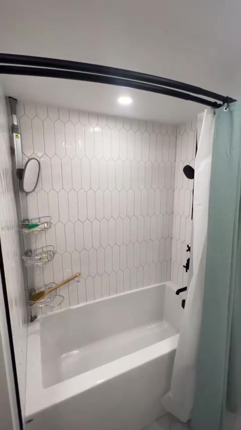 Vertically arranged elongated hexagonal tiles line this tub surround, finished with dark shower fittings.