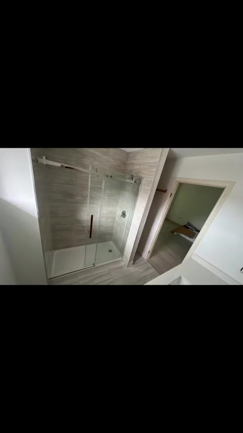 Stone-look rectangular wall tiles enclose a walk-in shower behind clear glass.