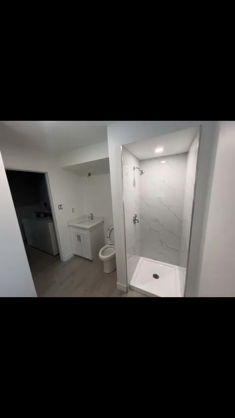 Pale veined shower walls sit beside a white vanity in this compact bathroom.