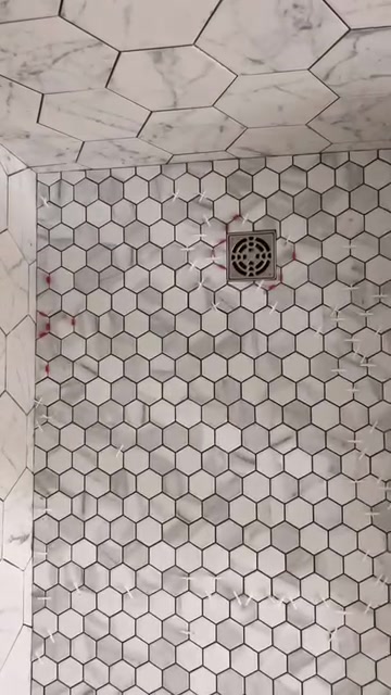 Small white hexagonal floor tiles and a square drain meet a larger marble-look hexagonal wall pattern.
