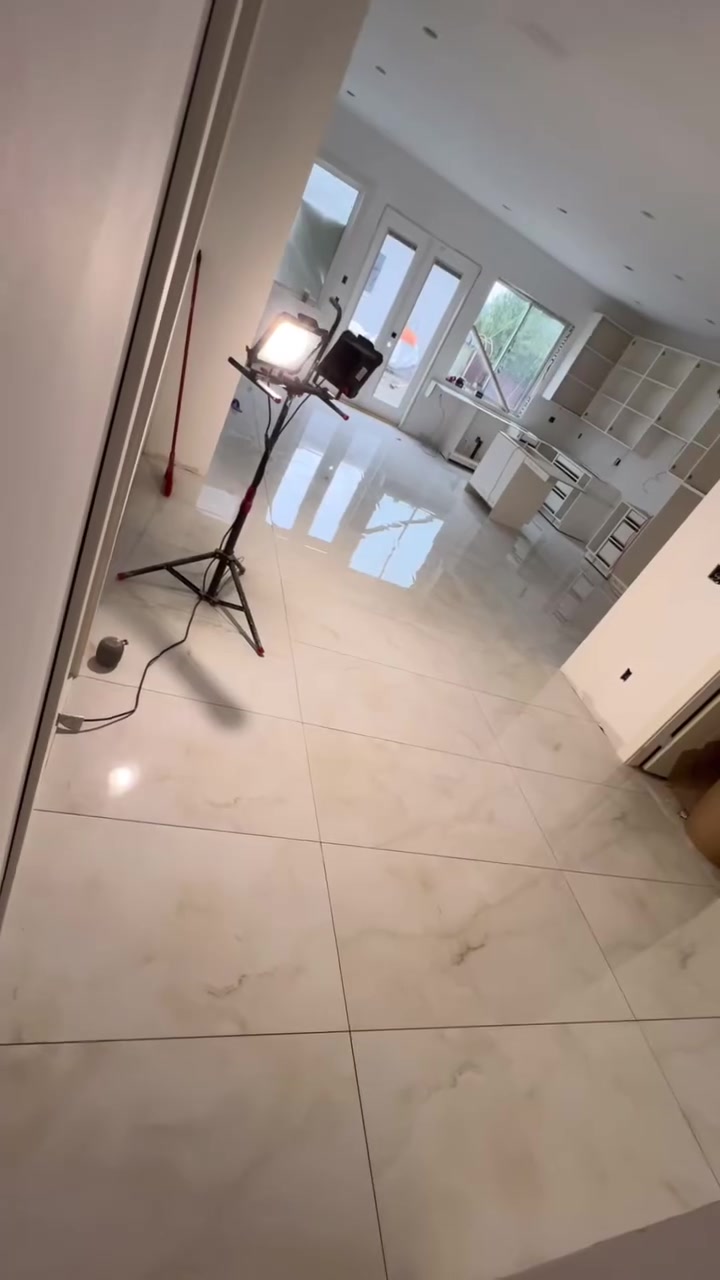 Large, glossy marble-look tiles extend down the hall into a bright living area. Shown during renovation.
