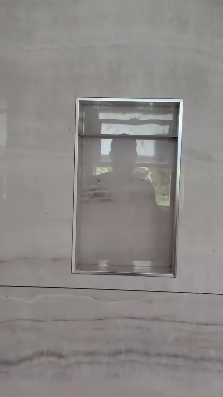 A tall rectangular niche with metal trim is set into gently striated, stone-look wall tiles.